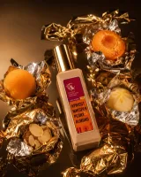 Натюрморт у вечірньому стилі: флакон Apricot Whisper, розкрита абрикосова половинка, листя тютюну, шматок темної шкіри і ветиверні гілки на теплому бурштиновому камені при низькому світлі