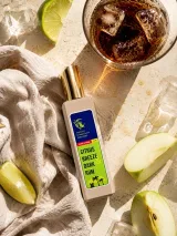 Долоня з флаконом Citrus Breeze на тлі шкіряних аксесуарів, годинника і вовняного пальта — деревно-амбровий шлейф у вечірньому золотистому світлі