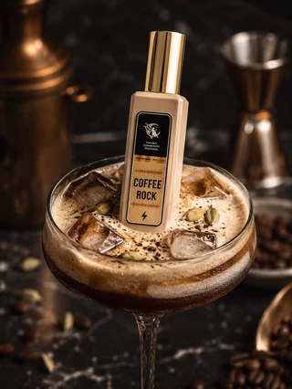 Натюрморт при контрастному світлі: флакон Coffee Rock, керамічна піала зі свіжемеленою арабікою, поряд зелені кавові зерна, коробочки кардамону і фрагмент темного дерева на графітовому камені